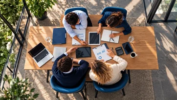 Bovenaanzicht van collega's die samenwerken aan een tafel met laptops